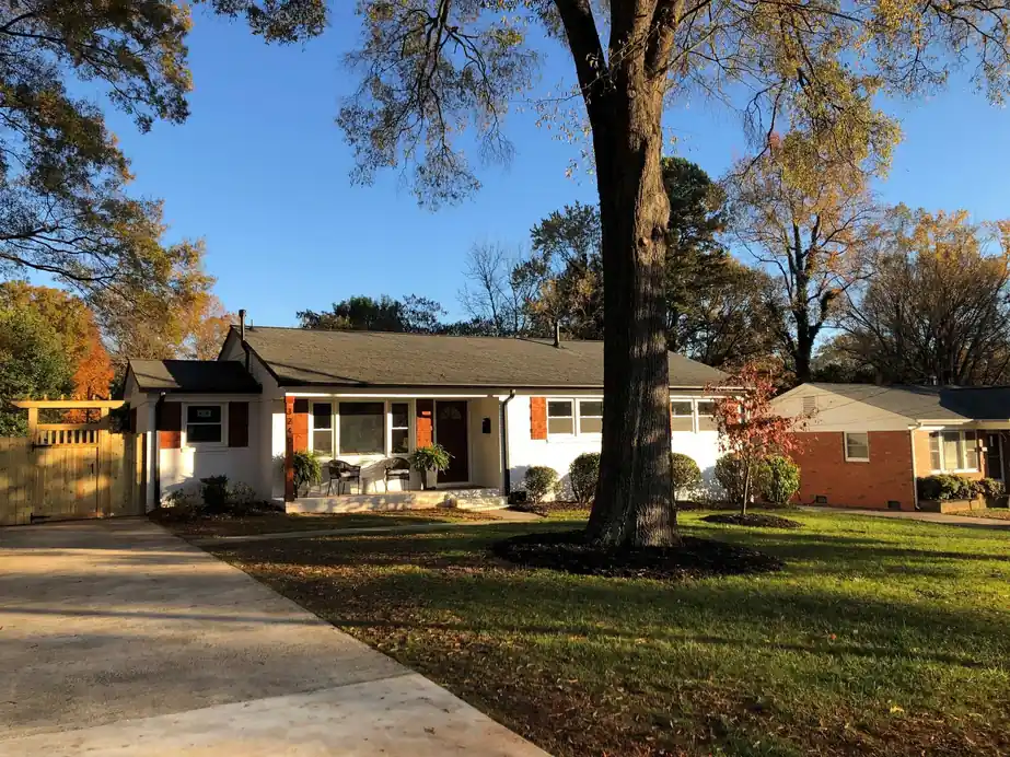 Front of a white ranch house under a mature tree in autumn light