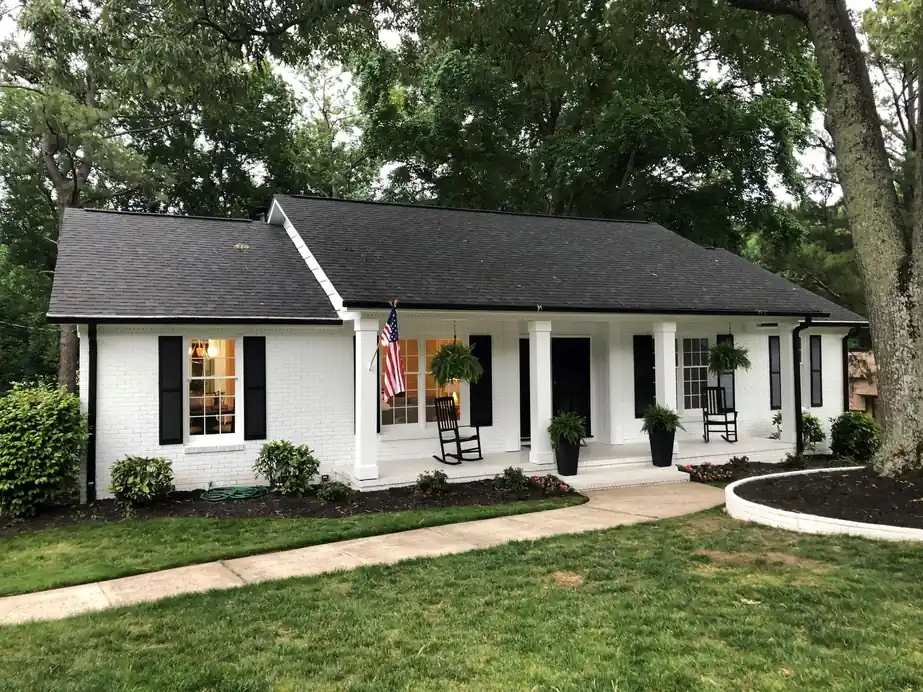 White-painted brick ranch with black shutters, a columned porch and a flag by the door