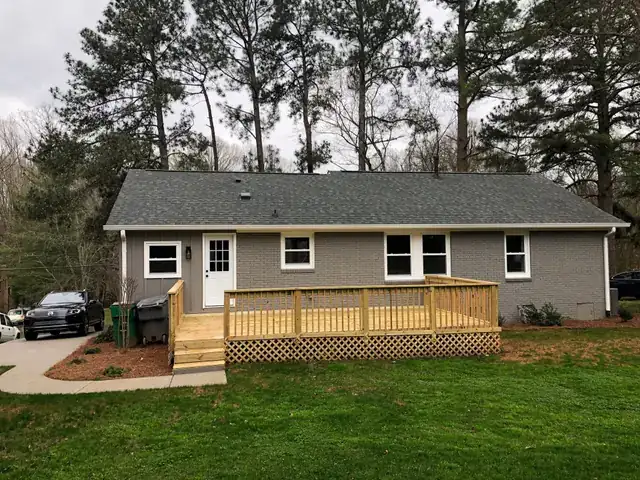 Rear of a grey brick ranch house with a new wood deck and steps down to the lawn