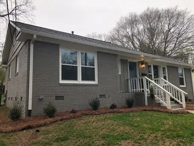 Side of a grey brick ranch house with a new white porch railing